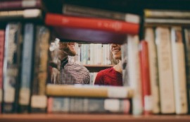 Imagen de dos estudiantes tras una pila de libros