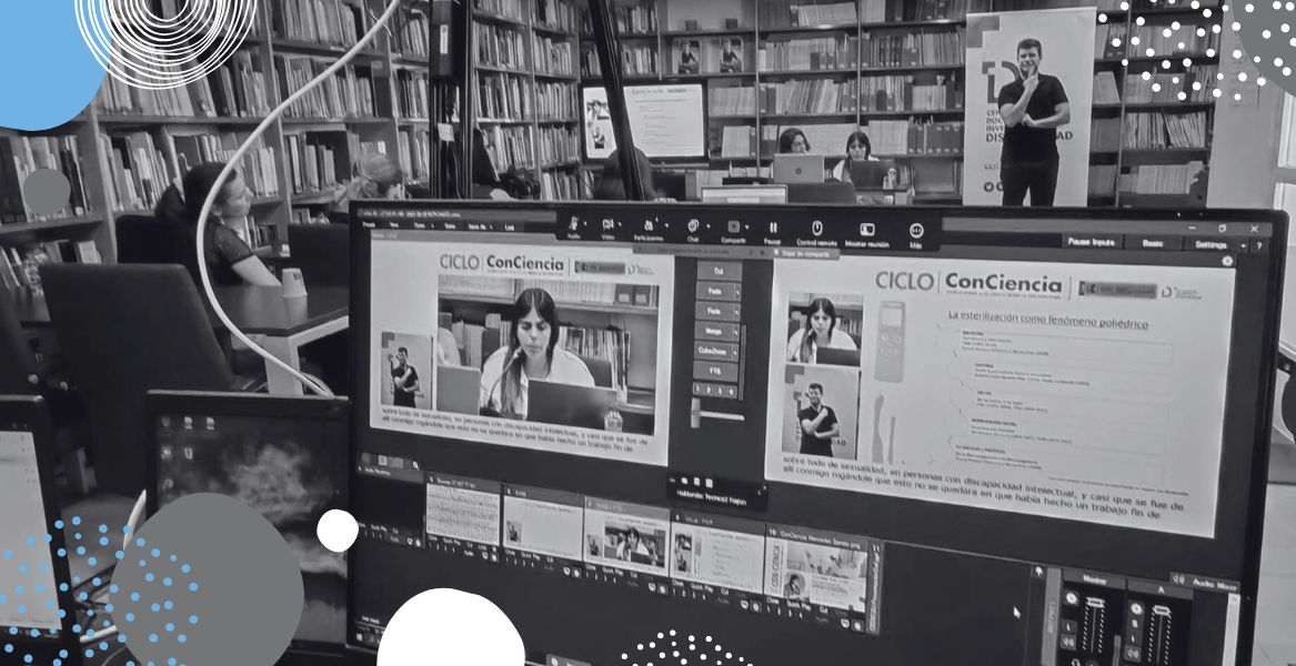 Fotograf&iacute;a de la pantalla de la emisi&oacute;n en directo del evento, con la sala de la biblioteca del CEDID al fondo con p&uacute;blico y ponentes.