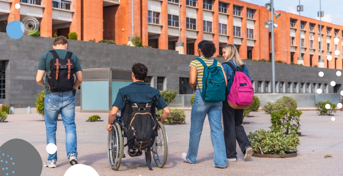 Foto de un grupo de alumnos, uno de ellos usuario de silla de ruedas, frente a una facultad
